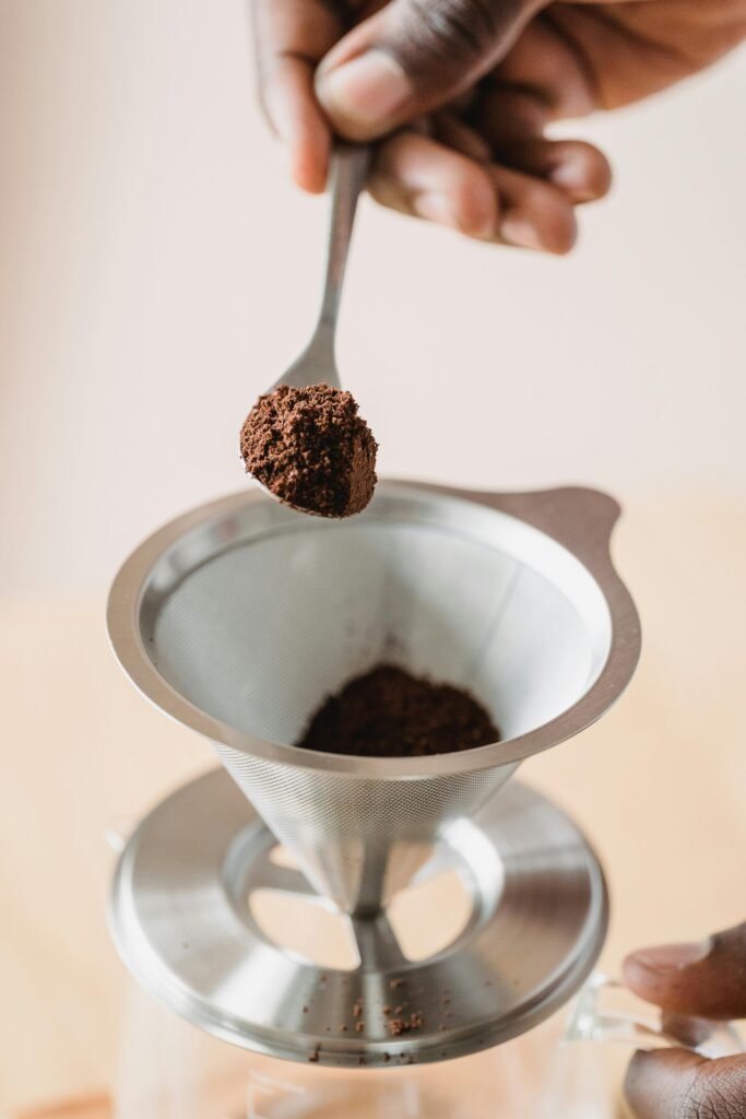 Detailed close-up of coffee grounds being spooned into a filter by hand, perfect for coffee enthusiasts.