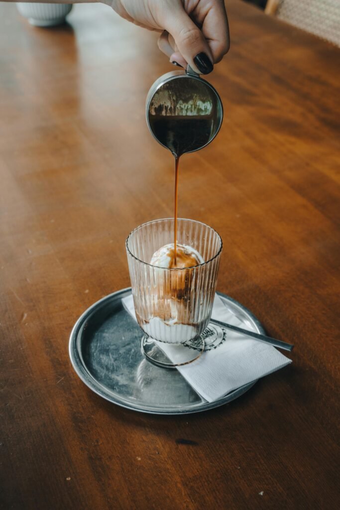 Close-up of an ice cream parfait in a glass with coffee being poured over it, creating a delectable dessert moment.