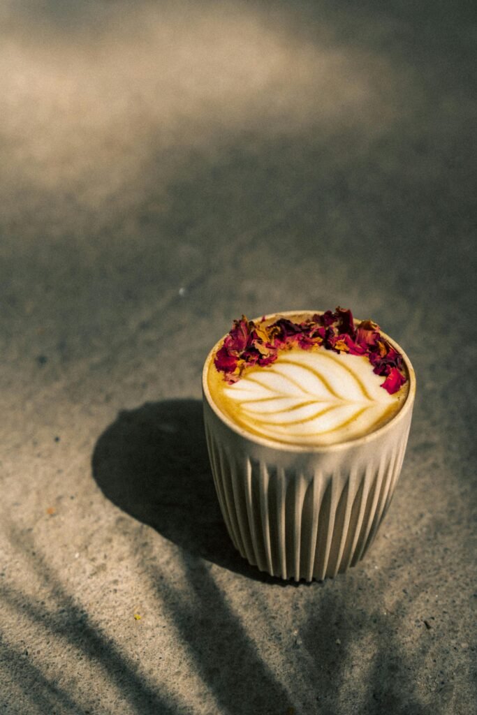 A latte with latte art and rose petals set on a textured surface, captured in natural light.