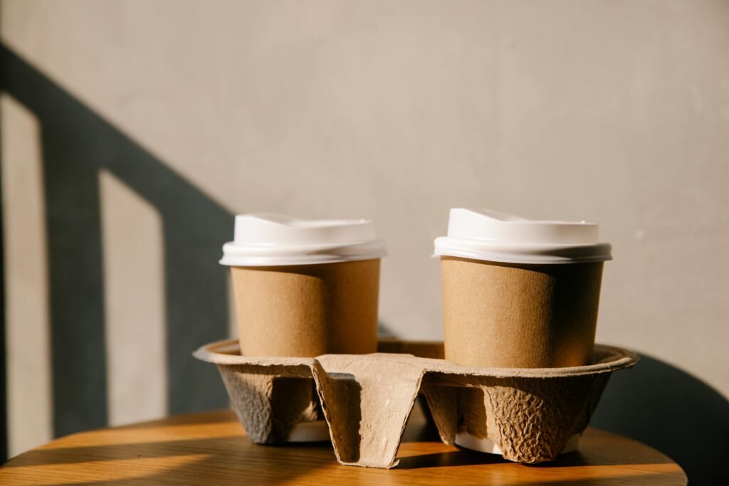 Two disposable coffee cups on a table with soft sunlight creating shadows, emphasizing eco-friendly packaging.