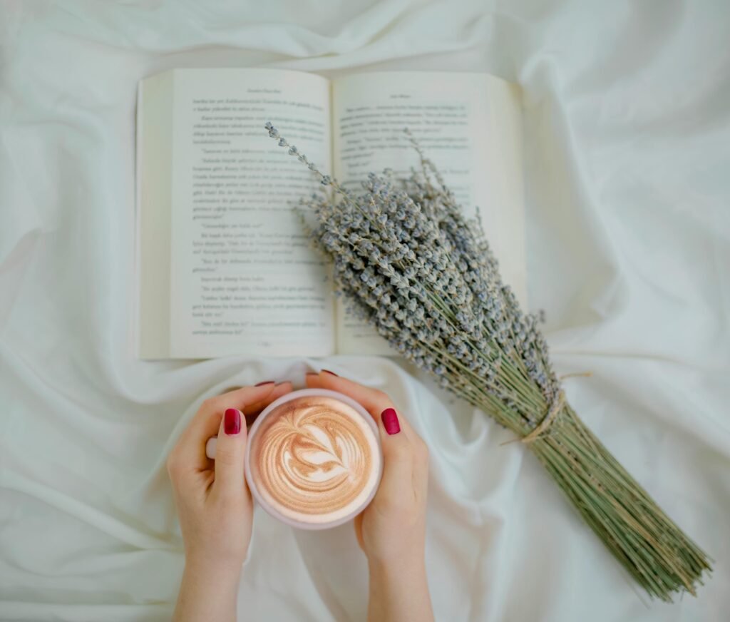 Hands holding a latte with lavender and an open book. Perfect cozy setting for relaxation.