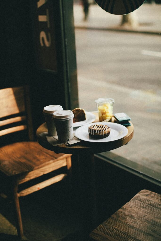 Warm lighting in a modern café with coffee, pastries, and wooden furniture by the window.