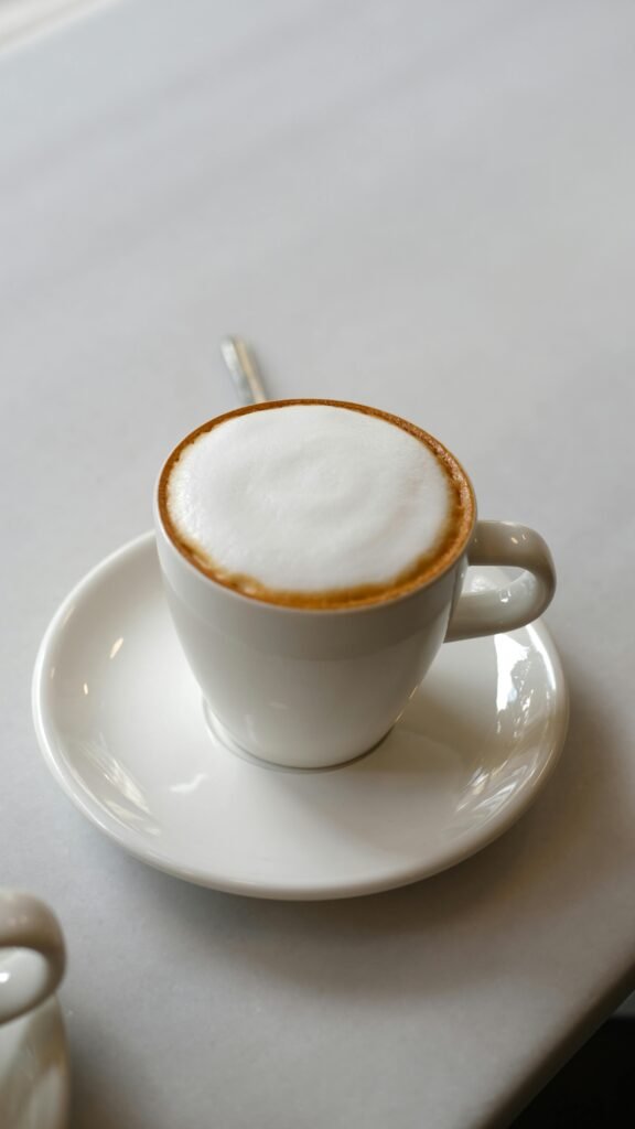 A steaming cup of cappuccino with frothy milk in a white porcelain cup on a saucer.