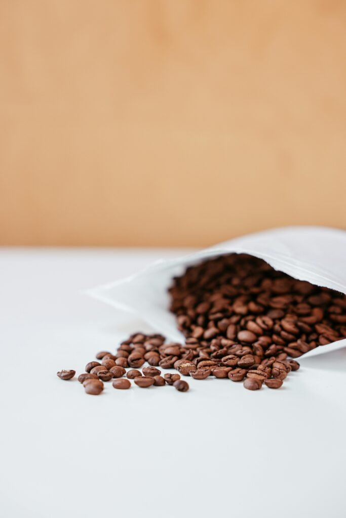 High-quality roasted coffee beans spilling from a white bag on a smooth surface.