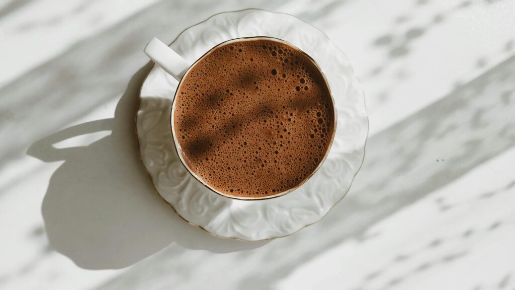 Aerial view of a foamy coffee in an ornate ceramic cup with sunlight.