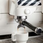 Close-up of espresso machine brewing fresh coffee into a white porcelain cup in a café.