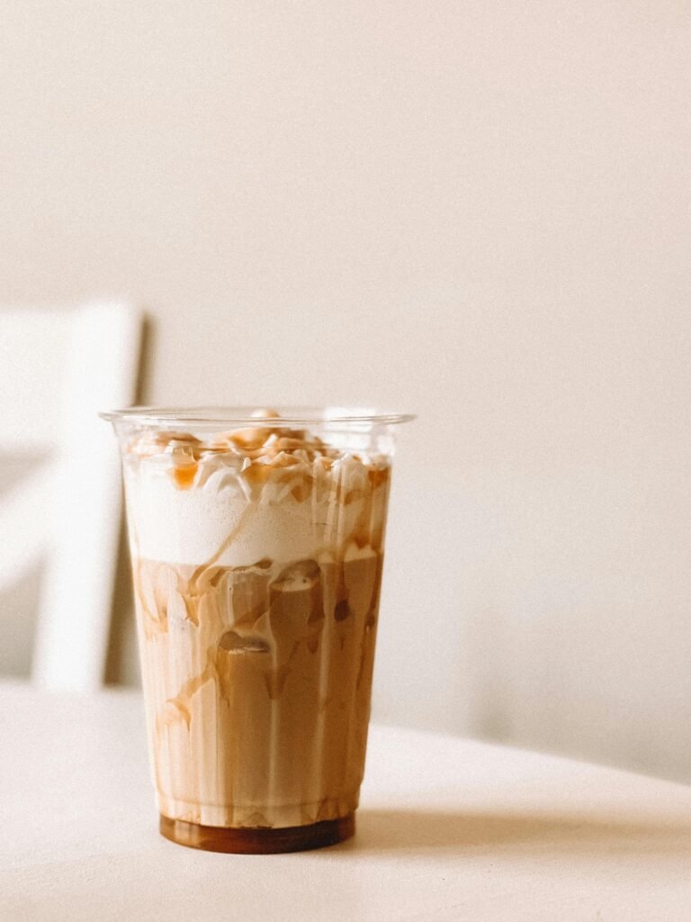 A refreshing iced creme brulee latte in a clear plastic cup on a table with a neutral background.