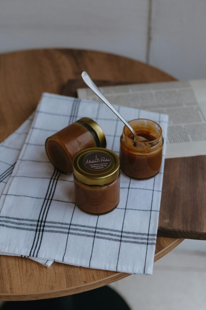 Two jars of caramel with a spoon on a wooden table, creating a cozy kitchen setting.