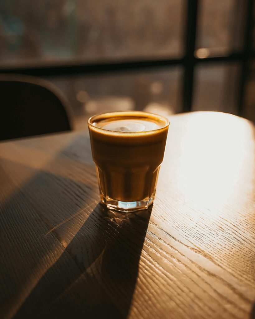 A cozy cappuccino glows in the warm sunset light on a wooden table, inviting relaxation.