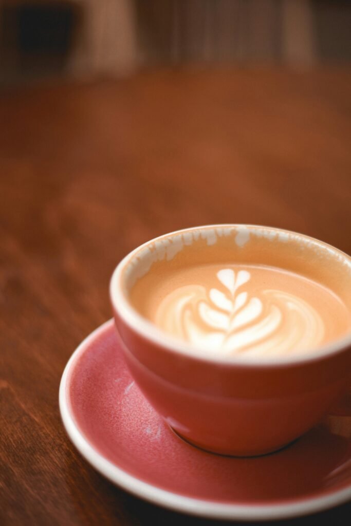 Close-up of a latte with latte art in a rustic pink mug on a wooden table.